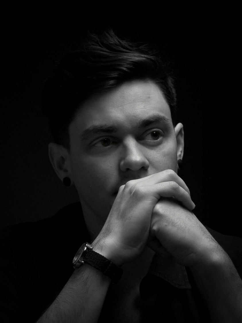 Black and white headshot of Peter looking off camera, resting his head on folded hands